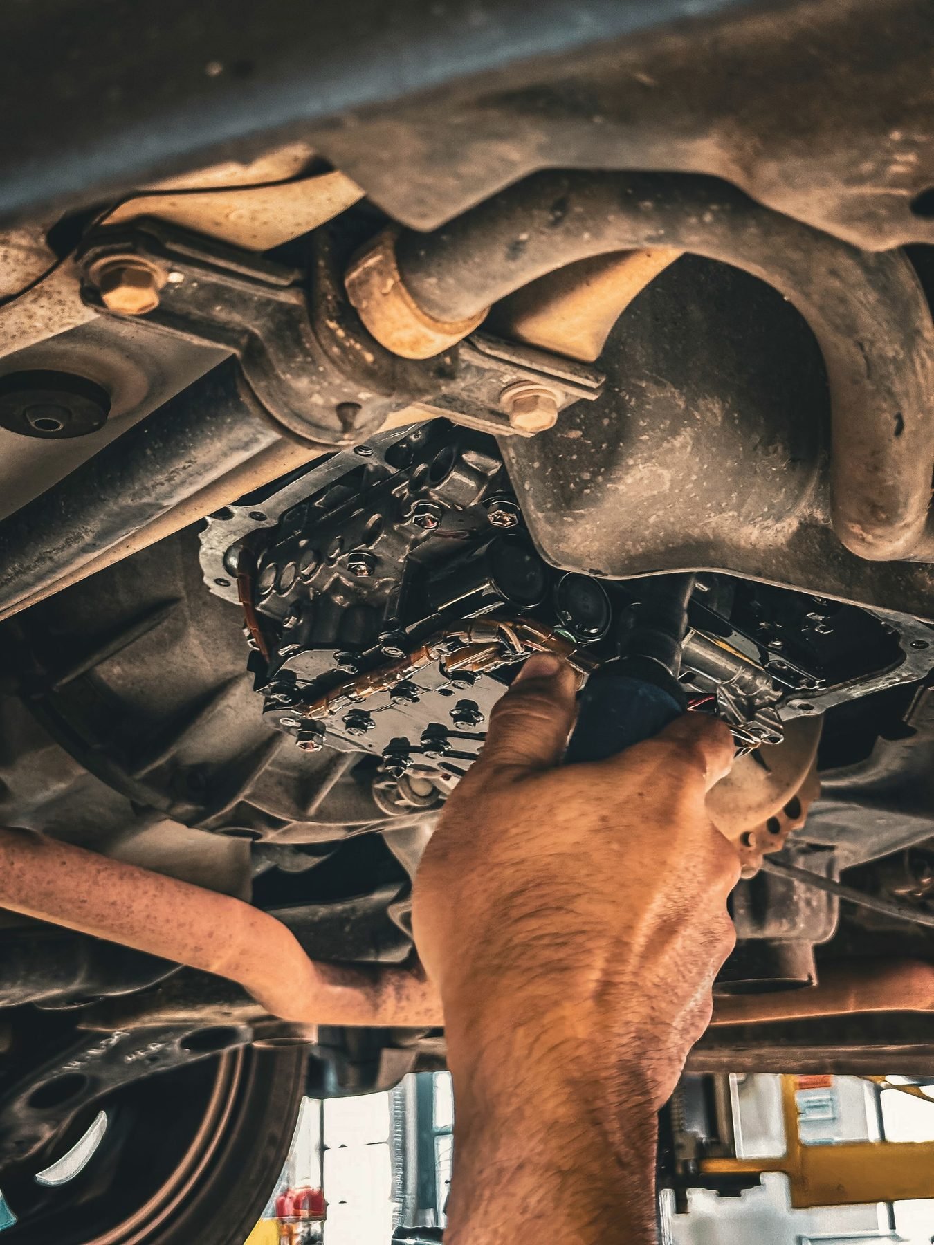 A hand reaching up to the underside of a car near the transmission